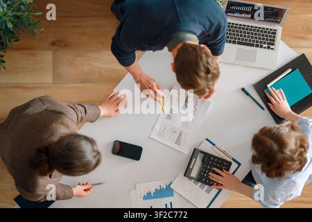 Dynamische Topansicht eines vielfältigen Geschäftsteams, das gemeinsam um einen Tisch arbeitet, Finanzdiagramme analysiert, Wachstumsstrategien diskutiert und Moderation verwendet Stockfoto