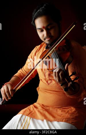 Ein Musiker in traditioneller Kleidung spielt mit ruhigem Ausdruck die Geige. Das warme Licht verleiht einen künstlerischen Touch und vermittelt Hingabe und Stockfoto