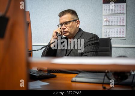Ernster Geschäftsmann telefoniert an einem Festnetztelefon, während er an seinem Bürotisch arbeitet. Professionelle Kommunikation, Geschäftsverhandlungen, Büromanagement Stockfoto