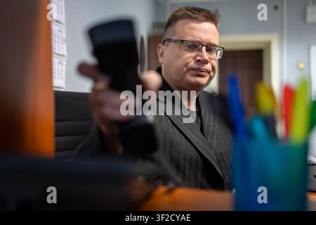 Mittelalternder Geschäftsmann mit Brille, der den schwarzen Telefonhörer entgegenhält. Stockfoto
