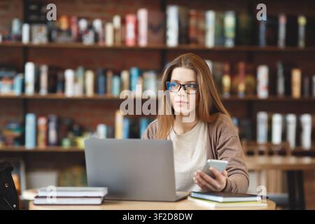 Nachdenklich Brünette Mädchen mit Laptop und Smartphone und Blick zur Seite Stockfoto