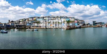 Panoramatische Ansicht des Brixham Harbour in Devon, England, mit farbenfrohen Hügelhäusern, Fischerbooten und einem hellen Sommerhimmel. Stockfoto