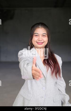 Eine vertikale Mittelaufnahme einer jungen südostasiatischen thailändischen Isan-Geschäftsfrau, die direkt in die Kamera lächelt, während sie ihre Hand nach vorne ausstreckt, um zu begrüßen Stockfoto