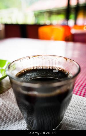 Frisch gebrühter schwarzer Kaffee, serviert in einer klaren Glas Tasse auf einem roten karierten Tischtuch Stockfoto