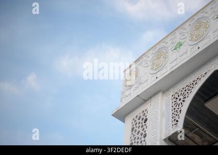 Detaillierte Ansicht eines eleganten weißen Architekturbogens mit aufwendigen islamischen geometrischen Mustern unter einem klaren Himmel Stockfoto