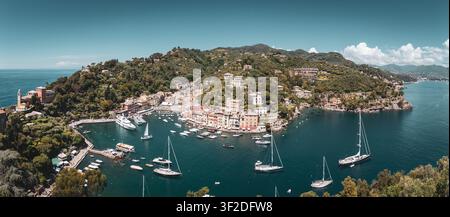 Panoramablick auf das wunderschöne Portofino an einem Frühlingsnachmittag mit Hafen, Booten, Yachten, Uferpromenade, Villen, grüne Hügel und klares blaues Wasser an der ligurischen Küste in Italien vor blauem Himmel Stockfoto