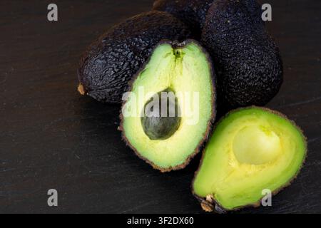 Hass-Avocado-Hälfte Nahaufnahme, ganze Sharwil, braune Avocados geschnitten, frische Alligatorbirne, Guacamole-Zutat, Persea-Americana-Avocado-Frucht-Nahaufnahme Stockfoto
