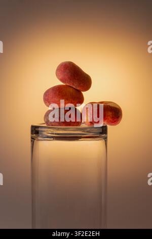 Flache Pfirsiche gestapelt oben und in einem Gläser im warmen goldenen Studiolicht. Kreative Obst- und Glaswarenkomposition, warme Herbsttöne, Kopierraum Stockfoto