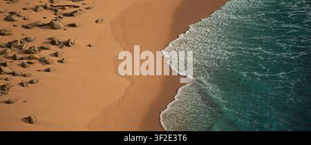 Luftbild eines sandigen Strandes mit verstreuten Felsen und türkisfarbenen Meereswellen, die an die Küste schwappen. Stockfoto