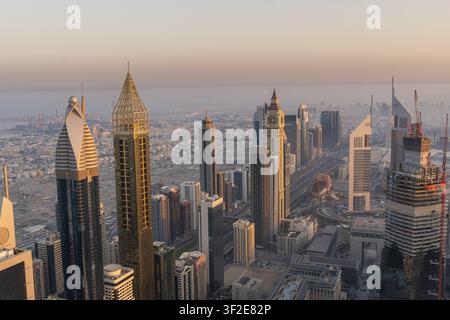 Luftbild der modernen Wolkenkratzer entlang der Sheikh Zayed Road in Dubai während der Goldenen Stunde, das die dichte urbane Architektur und die belebte Autobahn zeigt Stockfoto