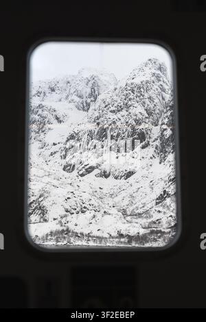 Schneebedeckte Berge der Lofoten-Inseln, die durch einen Fensterrahmen sichtbar sind und eine atemberaubende Winterlandschaft präsentieren. Die Szene zeigt die ruhige Schönheit Stockfoto