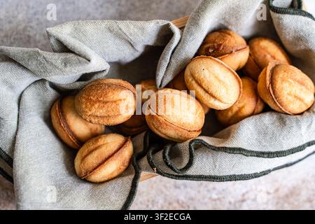 Goldene hausgemachte Nusskekse in Walnussform, eingebettet in ein rustikales Leinentuch auf einem Holztray. Gemütliche Dessertstilleben mit knusprigem gebackenem Gebäck und Stockfoto