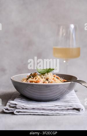 Rustikale Schüssel mit Tortellini-Pasta, gewürzt mit Kräutern und Gemüse, überzogen mit geriebenem Parmesan und frischem Basilikum, serviert mit einer Gabel und einem Glas Weißwein Stockfoto