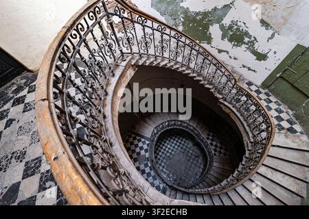 Faszinierender Blick auf eine kunstvolle Wendeltreppe in einem verlassenen Gebäude. Ihr filigranes Eisengeländer und die verwitterten Stufen spiegeln den Charme und die Geschichte wider Stockfoto