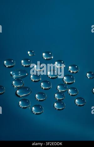 Makroaufnahme von klaren Wassertropfen auf Glas, die glänzende Perlen mit hellen Reflexionen vor einem tiefblauen Hintergrund bilden. Minimale abstrakte Textur für ra Stockfoto