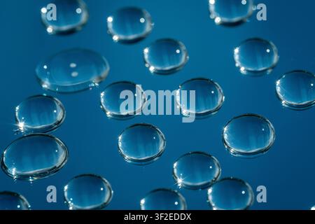 Nahaufnahme-Makroaufnahme von klaren Wassertropfen auf Glas, die glänzende runde Perlen mit hellen Reflexionen auf einem tiefblauen abstrakten Hintergrund für Text bilden Stockfoto