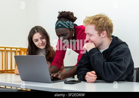 Multikulturelle Studentengruppe studiert gemeinsam in einem Klassenzimmer, kollaboriert an einem Laptop mit konzentrierter Diskussion, Teamarbeit und gemeinsamem Lernen an einem m Stockfoto