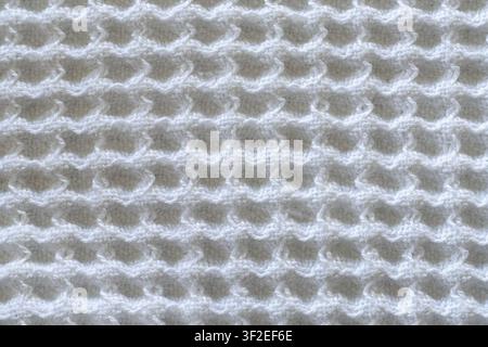 Eine Nahaufnahme zeigt einen weißen Strickstoff mit einem sich wiederholenden welligen Muster. Die Textur wirkt weich und leicht erhaben, was einen räumlichen Effekt erzeugt Stockfoto
