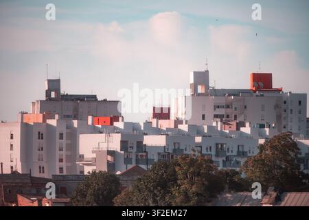 Komprimierte Teleobjektivansicht von geschichteten Wohnblocks mit weißen und roten Dachkonstruktionen, Antennen und Schornsteinen, die im warmen Sonnenlicht unter dem Himmel leuchten Stockfoto