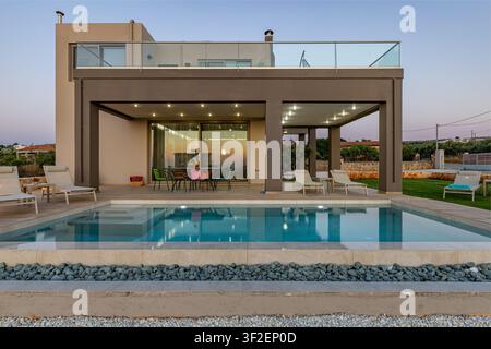 Blick auf eine moderne Villa mit einem Schwimmbecken, einem Außen-Essbereich und Liegestühlen in Chania, Griechenland. Stockfoto