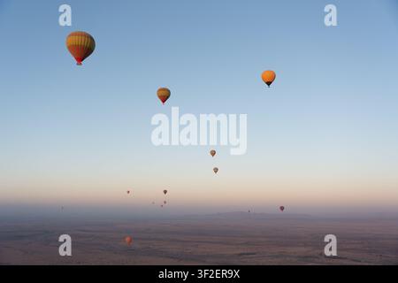 Blick auf mehrere farbenfrohe Heißluftballons, die bei Sonnenaufgang über die weite Wüstenlandschaft nahe Marrakesch, Marrakesch-Safi, Marokko schweben. Stockfoto