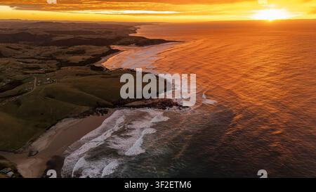 Drohnen-Luftbild eines spektakulären goldenen Sonnenaufgangs, der die raue Wildküste an der Ostkap-Küste in Südafrika beleuchtet. Sanfte grüne Hügel, Stockfoto