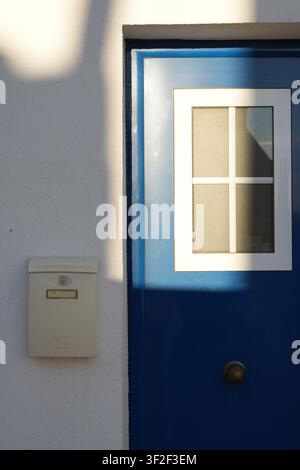 Eine traditionell blau gestrichene Tür mit einem weiß gerahmten Fenster und einem kleinen an der Wand montierten Briefkasten, typisch für europäische Wohnarchitektur Stockfoto