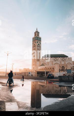 Casablanca, Casablanca-Settat, Marokko - 15. November 2025: Blick auf die Hassan-II-Moschee mit ihrem Minarett, das sich in einer Straßentümpel widerspiegelt, mit einem Motorrad Stockfoto