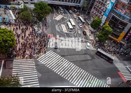 Hohe Blickwinkelansicht der berühmten Shibuya-Kreuzung, die Menschenmassen auf den Bürgersteigen, Zebrastreifen, vorbeifahrende Busse, eine Stockfoto