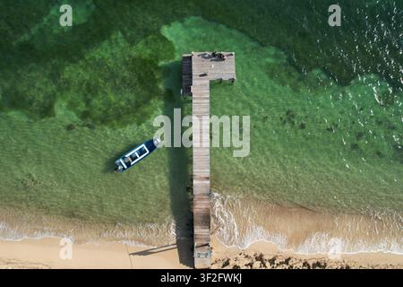 Luftbild eines hölzernen Piers, der sich in das klare türkisfarbene Wasser der Karibik erstreckt, mit einem kleinen Boot, das neben dem sandigen Strand in Coxe festgemacht ist Stockfoto