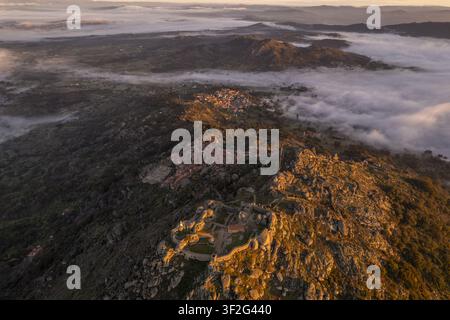 Luftbild des historischen Schlosses von Monsanto, das auf einer felsigen Hügelkuppe thront und das Dorf Monsanto überblickt, umgeben von Morgennebel in Monsanto, C Stockfoto