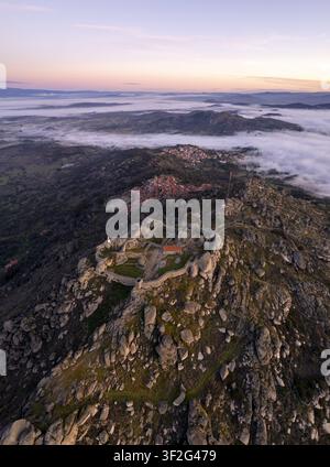 Luftaufnahme der Ruinen des Monsanto-Schlosses, das auf einer felsigen Hügelkuppe thront, umgeben von Morgennebel und sanften Hügeln bei Sonnenaufgang in Monsanto, Castelo Branco Di Stockfoto