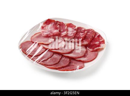 Sortiment an geschnittenem Schink und Salami auf einem weißen Teller, in Plastikfolie eingewickelt, isoliert auf weißem Hintergrund Stockfoto
