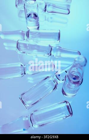 Gruppe leerer Glas-Medizinampullen auf blauer reflektierender Oberfläche Stockfoto