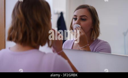 Frau verwendet ein Wattepad für die Gesichtspflege an ihrem Badezimmerspiegel Stockfoto