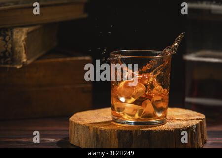 Whisky spritzt aus dem Glas mit Eiswürfeln in einer gemütlichen Umgebung Stockfoto