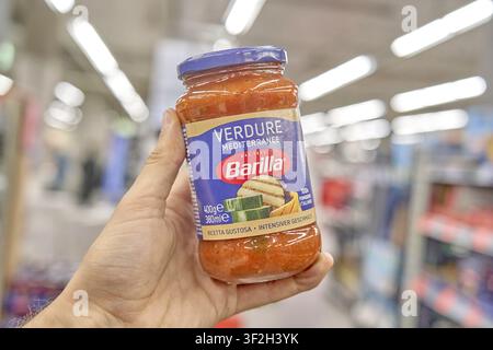 Mediterrane Vegetation, ein Glas Barilla Verdure-Tomatensoße wird in einer Hand gehalten, Supermarkt im Hintergrund, Tomatensoße in einem Glas, Produkt von Stockfoto
