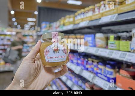 Ein Glas Manuka-Honig wird in der Hand gehalten, im Hintergrund Regale mit anderen Produkten in einem Supermarkt, Lebensmittelprodukt, Lebensmittelladen, Supermarkt, R Stockfoto
