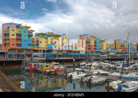 Gebäude in hellen Farben säumen den Yachthafen von Albufeira, wo verschiedene Boote festgemacht sind. Die Szene spielt sich unter einem bewölkten Himmel in einer Küstenstadt ab. Stockfoto