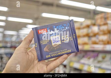 Dunkelblaue Verpackung mit elegantem Design und dunklen Schokoladenstücken im Hintergrund eines Supermarktregals, Rittersport-Schokolade, quadratischer Ritter Sport Stockfoto