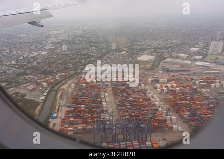 Frachtterminal mit Hunderten von bunten Schiffscontainern und großen Kränen, die die Landschaft durchziehen. Blick aus einem Flugzeugfenster über einer Ausdehnung Stockfoto