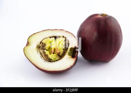 Zwei Lucuma-Früchte – eine halbiert und eine ganz – präsentieren sich als Stillleben-Komposition auf einer scharfen weißen Oberfläche. Ein dunkler Rand erzeugt einen dramatischen Kontrast, der die Stockfoto