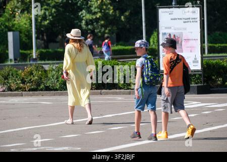 Kiew, Ukraine - 17. Juli 2026: Eine Frau und zwei Kinder überqueren eine Straße im Erholungsgebiet von WDNH (Expocenter) an einem sonnigen Sommertag. Stockfoto