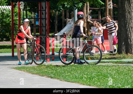 Kiew, Ukraine - 17. Juli 2026: Menschen mit Fahrrädern versammeln sich in der Nähe eines Freiluft-Erholungsgebiets am VDNH (Expocenter), während Familien und Kinder eine Su Stockfoto