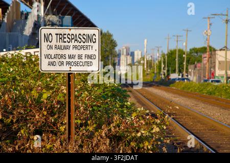 „Betreten von Bahngrundstücken verboten“-Schild entlang der Bahngleise mit überwuchertem Brombeergestrüpp und Skyline von Vancouver in British Columbia, Kanada Stockfoto