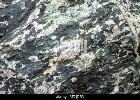 Detaillierte Nahaufnahme einer texturierten Felsoberfläche, die verschiedene Mineralmuster und Farben zeigt und die geologischen Merkmale und Texturen hervorhebt Stockfoto