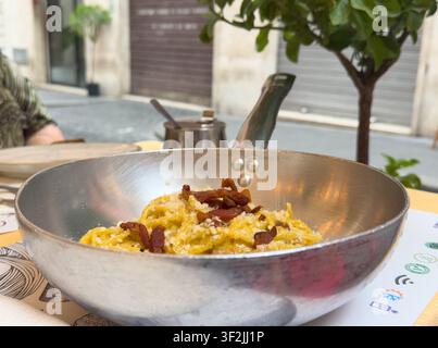 Authentische italienische Pasta Carbonara mit knusprigem Guanciale, serviert in einer traditionellen Metallpfanne auf einem Außentisch eines Restaurants in Rom, Italien. Stockfoto