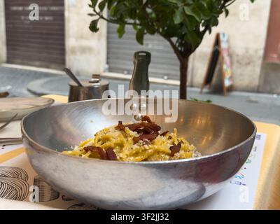 Authentische italienische Pasta Carbonara mit knusprigem Guanciale, serviert in einer traditionellen Metallpfanne auf einem Außentisch eines Restaurants in Rom, Italien. Stockfoto