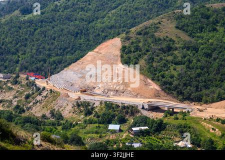 Große Baustelle an einem bewaldeten Hang. Erdarbeiten und Maschinen sichtbar. Straße im Bau schneidet sich durch grüne Landschaft Stockfoto