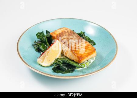 Gegrilltes Lachsfilet auf türkisfarbenem Teller mit Spinat-Zitronen-Erbsen auf weißem Hintergrund. Stockfoto
